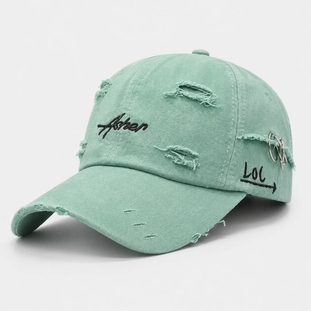 Josh & Tate - AsherLOL™ Distressed Cap - A distressed mint green baseball cap with frayed details, featuring black embroidered text on the front and side, and a silver ring accent on the side panel, set against a plain light gray background.