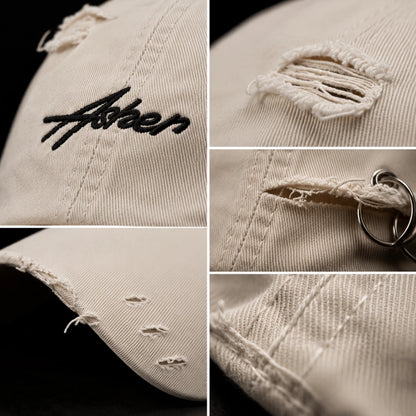 Josh & Tate - AsherLOL™ Distressed Cap - A beige distressed baseball cap shown in a four-panel close-up collage, highlighting black script embroidery, frayed ripped details, a metal keyring attachment, and the ribbed fabric texture against a black background.