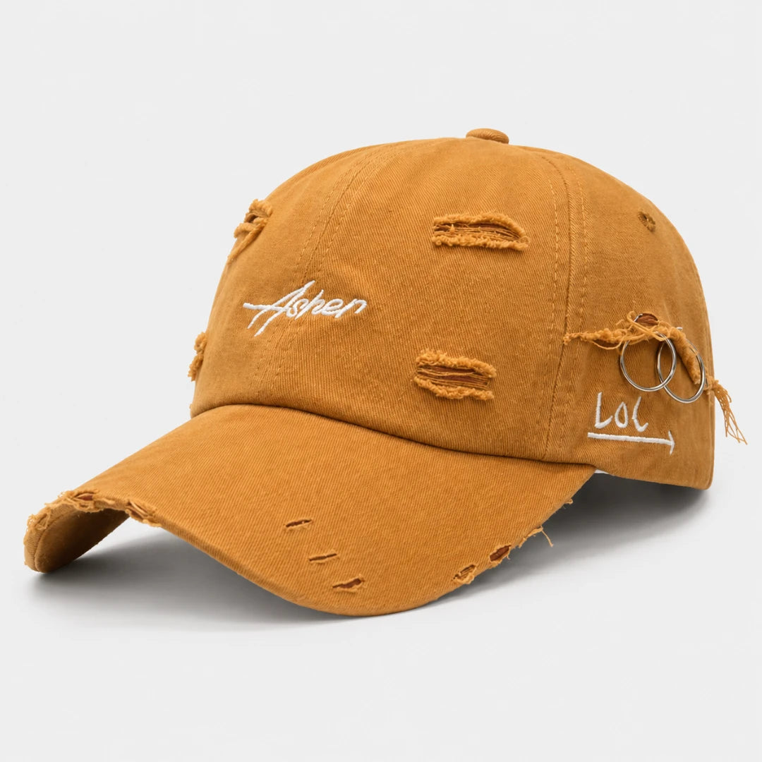 Josh & Tate - AsherLOL™ Distressed Cap - A distressed dad-style baseball cap in a washed mustard yellow color, featuring white embroidered text on the front and side ('Ashen' and 'Lol') with ripped details and frayed threads, set against a plain light gray background.