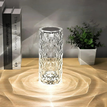 Crystal-like lamp on a wooden surface with a plant and books in the background