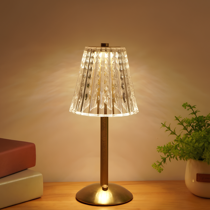 Table lamp with a clear glass shade on a wooden surface, emitting a warm glow.