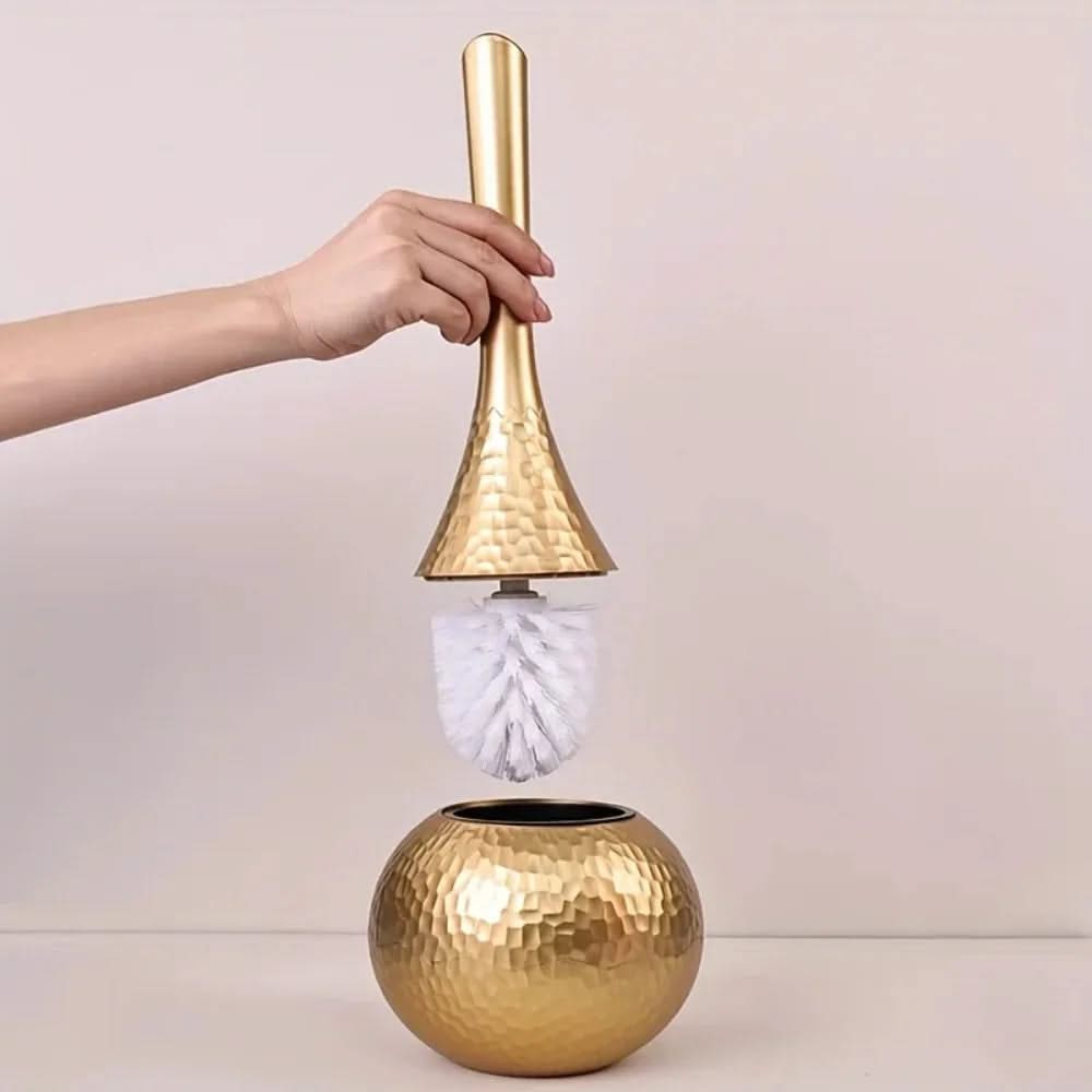 Gold cleaning brush with a white bristle head held by a hand against a light background