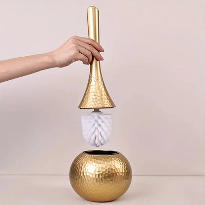 Gold cleaning brush with a white bristle head held by a hand against a light background