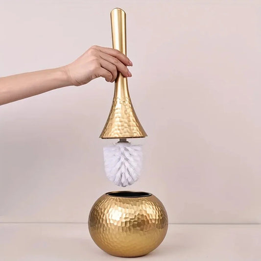 Gold cleaning brush with a white bristle head held by a hand against a light background