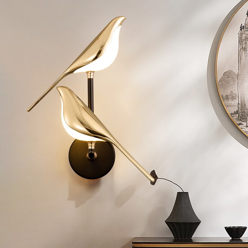 Gold bird-shaped wall lamp on a neutral wall with a framed picture.