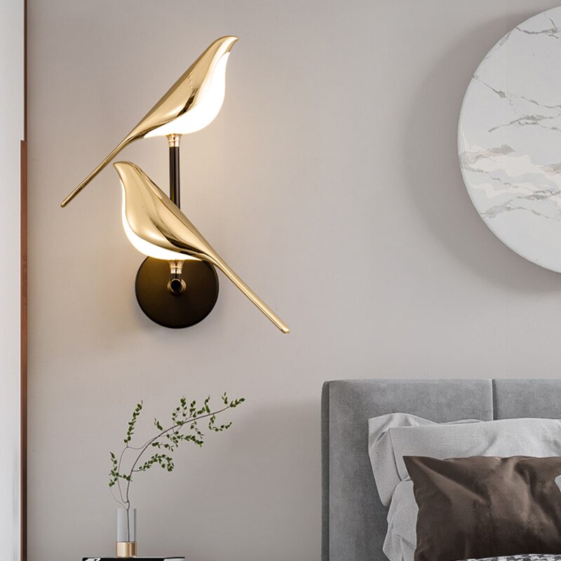 Gold bird-shaped wall lamp in a bedroom setting with a gray headboard and decorative pillow.