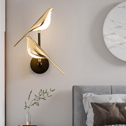 Gold bird-shaped wall lamp in a bedroom setting with a gray headboard and decorative pillow.