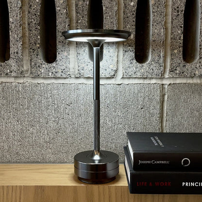 Black desk lamp on a wooden surface with a book titled 'Life & Work' by Joseph Campbell against a stone wall background.