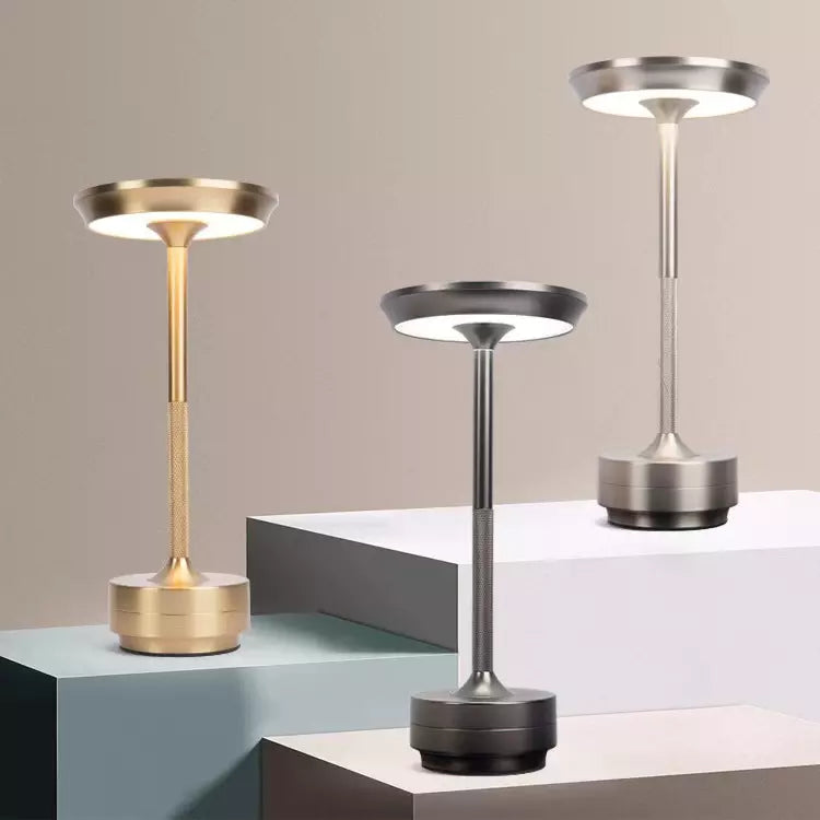 Three modern table lamps in gold, silver, and black on a geometric surface with a neutral background.