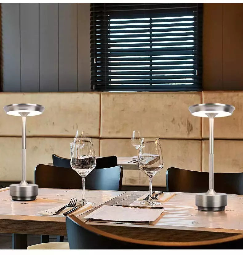 Two silver table lamps on a wooden dining table with glasses and cutlery.