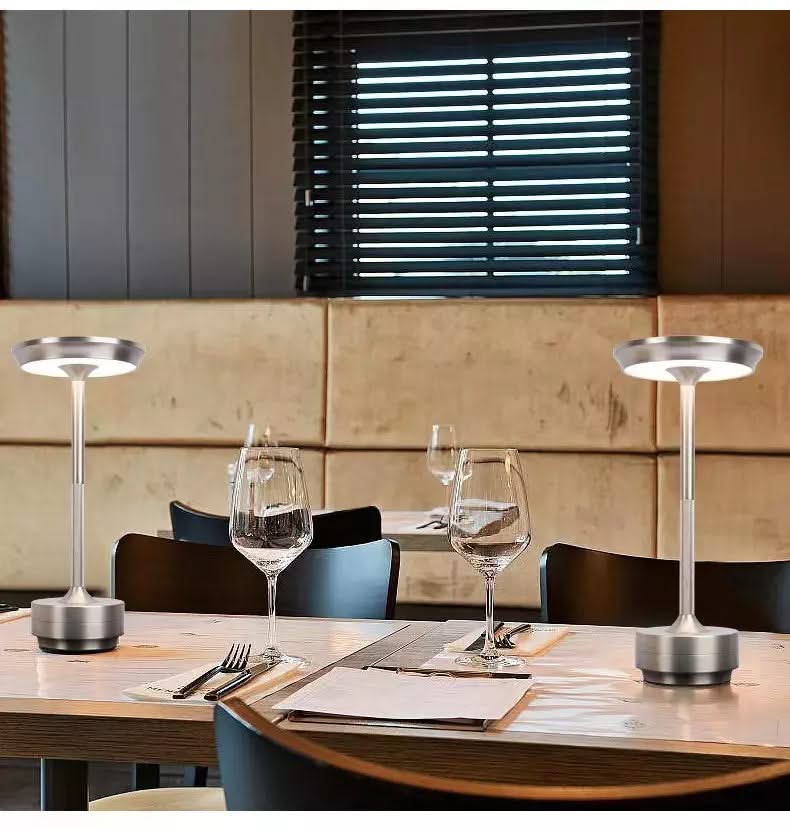 Two silver table lamps on a wooden dining table with glasses and cutlery.