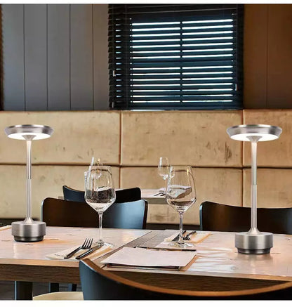 Two silver table lamps on a wooden dining table with glasses and cutlery.