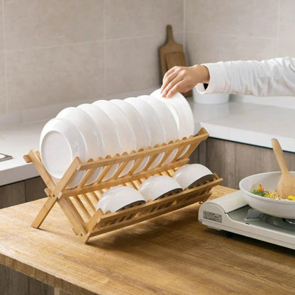 Person placing plates into a wooden dish rack on a kitchen counter.