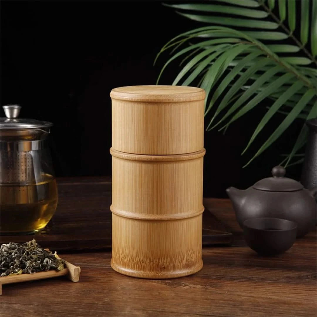 Josh & Tate - Bamboo Food Storage Container - Bamboo tea canister on a wooden surface with tea-making items and leaves in the background.