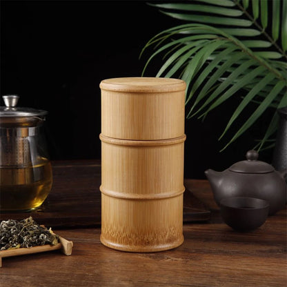 Josh & Tate - Bamboo Food Storage Container - Bamboo tea canister on a wooden surface with tea-making items and leaves in the background.
