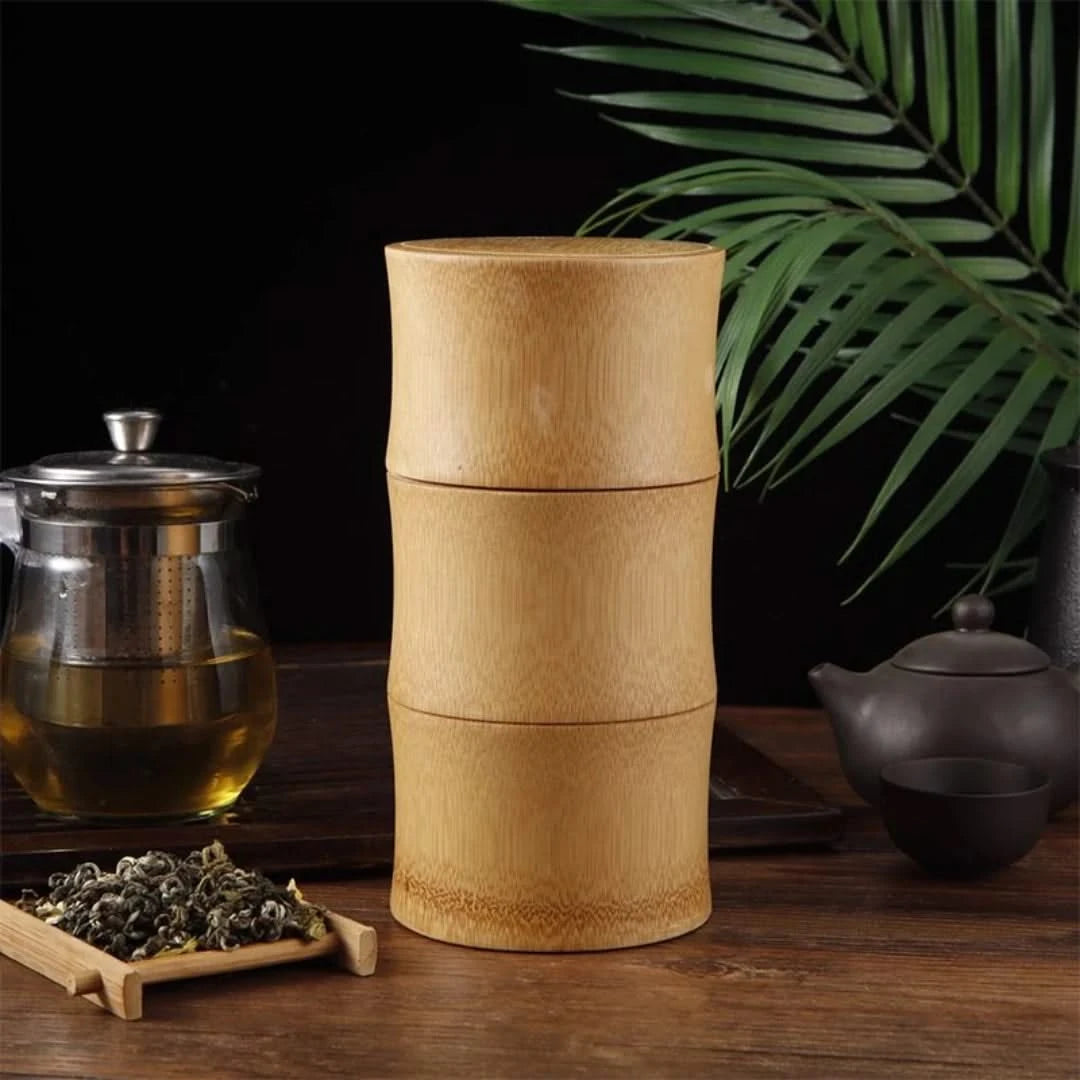 Josh & Tate - Bamboo Food Storage Container - Bamboo tea canister on a wooden table with tea-making items and leaves.