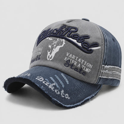 Josh & Tate - BlackRebel™ Distressed Cap - A distressed baseball cap with a gray front panel and a dark blue denim brim and side panels. The front features embroidered text reading 'Black Rebel' in dark blue, a white cowboy silhouette, and white text reading 'Dakota' and 'VARIATION AFTER A TLFMP State'.