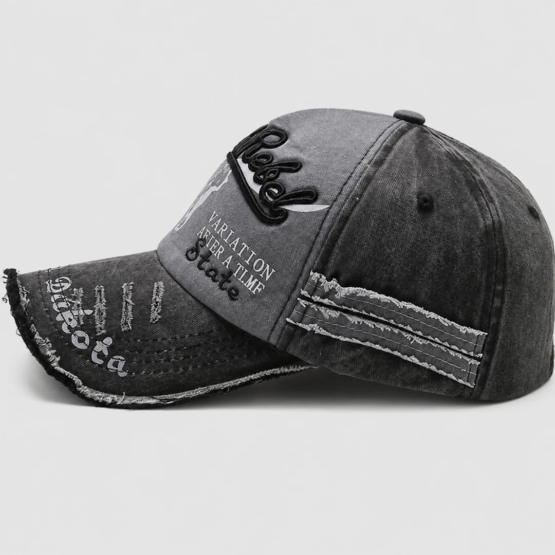 Josh & Tate - BlackRebel™ Distressed Cap - A dark gray washed denim baseball cap with distressed details, featuring black embroidered script on the front and white text on the brim, set against a light gray background.