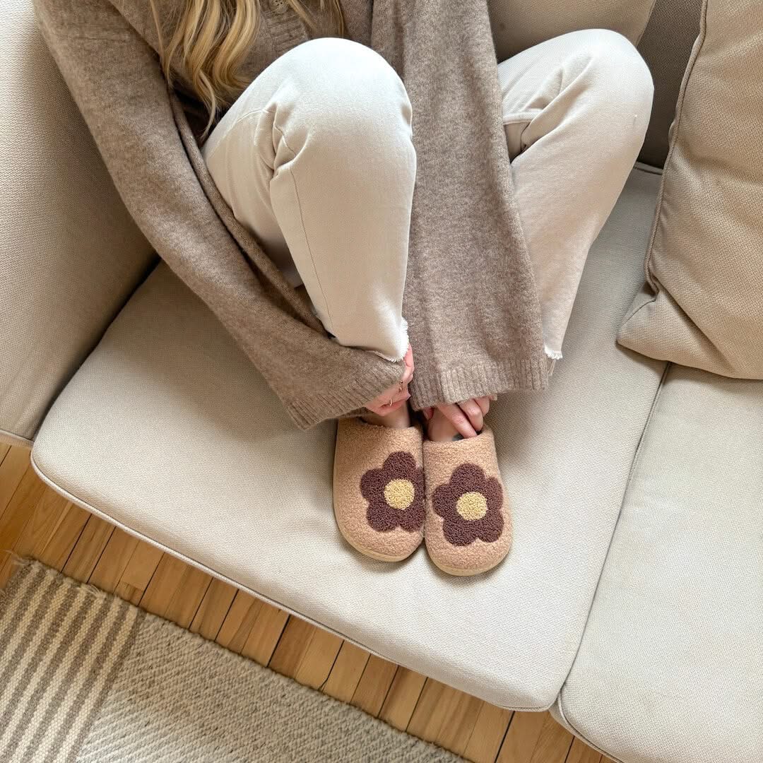 Person wearing beige slippers with flower design sitting on a couch.