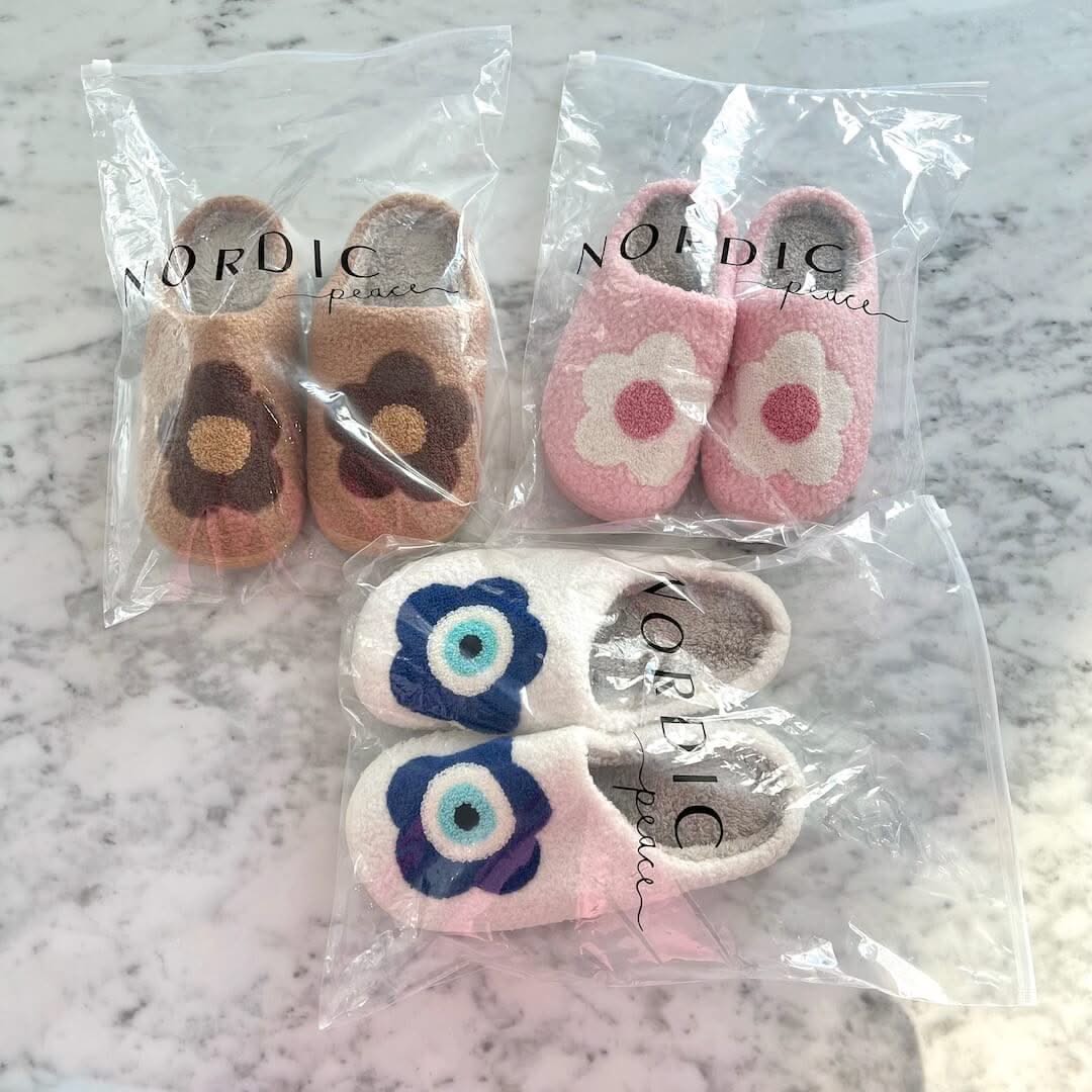 Set of children's slippers with floral designs in clear packaging on a marble surface.
