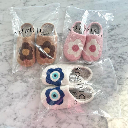 Set of children's slippers with floral designs in clear packaging on a marble surface.