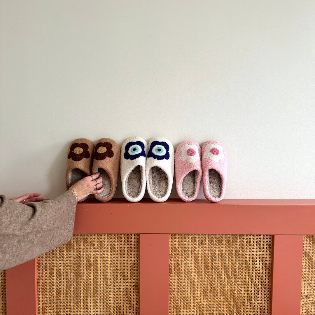 Four pairs of colorful slippers on a wooden shelf against a white wall.