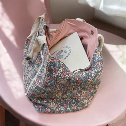 Josh & Tate - Blossom Tote Bag - Floral-patterned handbag with a pink umbrella and notebook on a pink chair.