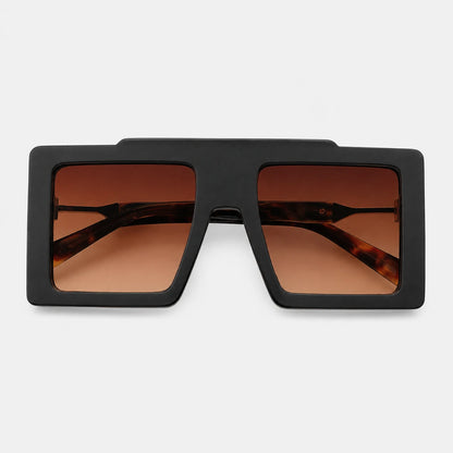 Josh & Ttate - BoldFrame™ Square Glasses - A pair of oversized square sunglasses with a matte black frame and warm brown gradient lenses, shown against a light gray background.