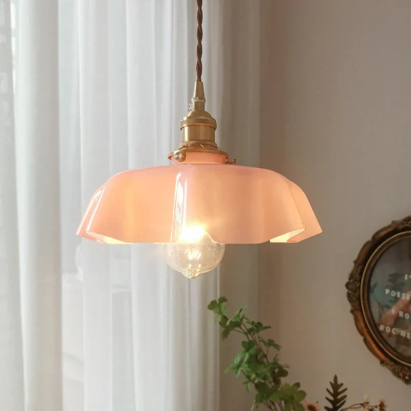 Pink pendant light with a gold fixture hanging in a room with white curtains and a decorative clock.