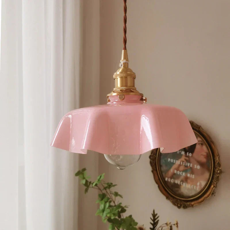 Pink pendant light with gold fixture on a neutral wall with a decorative mirror and plant.