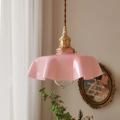 Pink pendant light with gold fixture on a neutral wall with a decorative mirror and plant.