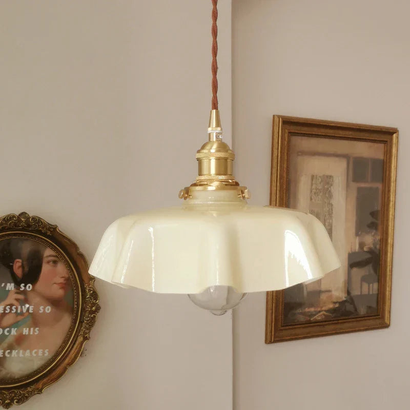 Vintage-style pendant light with a white glass shade and brass fitting against a wall with framed pictures.