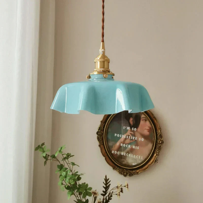 Light blue pendant lamp hanging on a beige wall with a decorative mirror and plant.