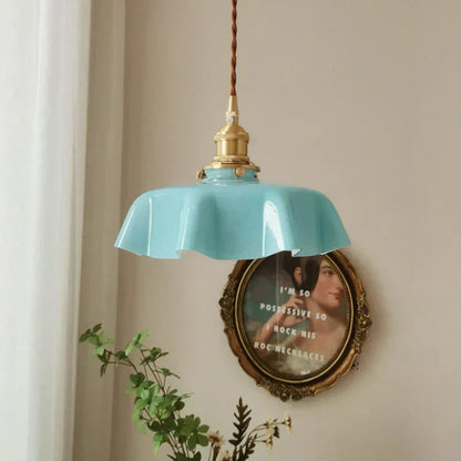 Light blue pendant lamp hanging on a beige wall with a decorative mirror and plant.