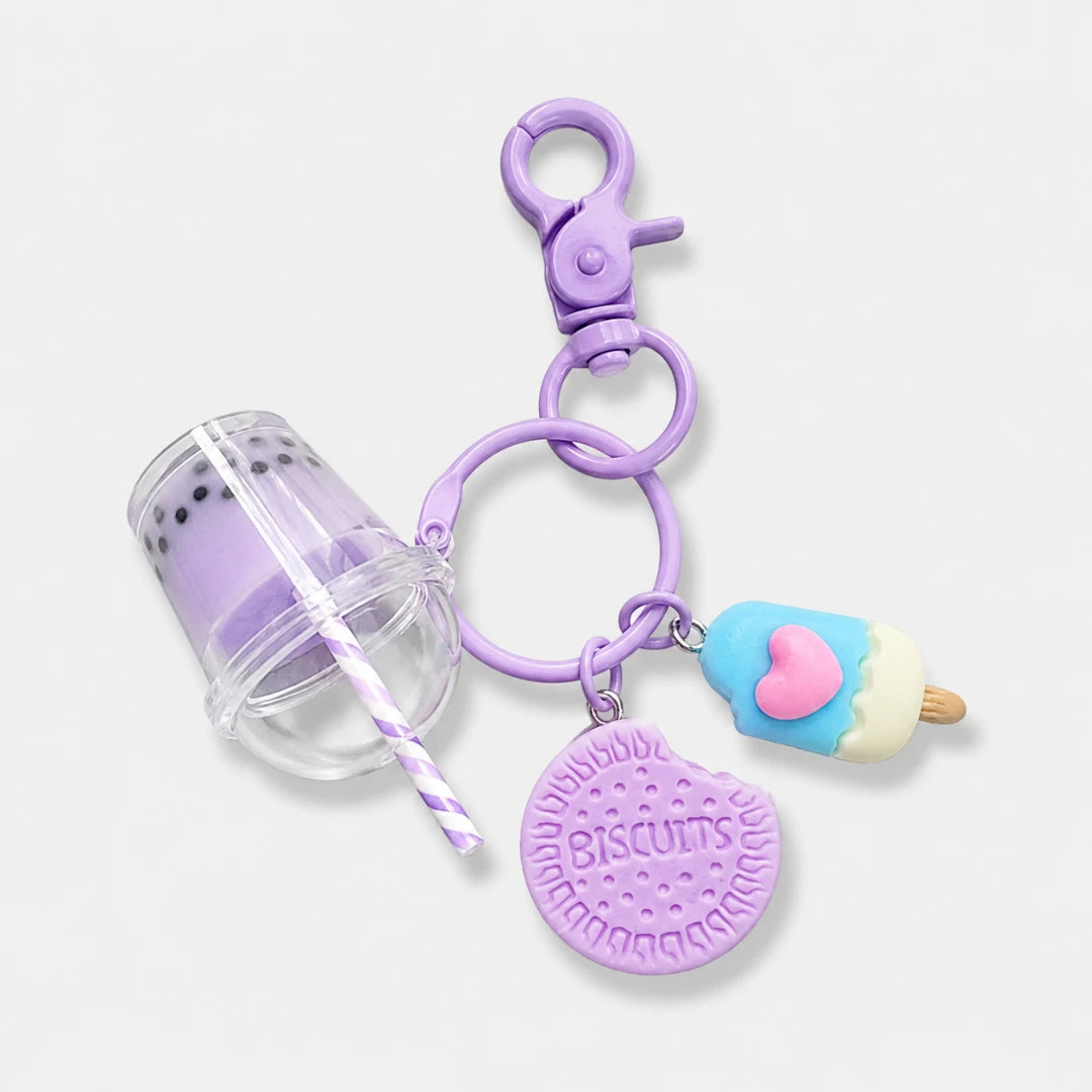 Josh & Tate - BubbleBite™ Milk Tea Keychain - A purple keychain featuring a clasp, a clear cup charm with a purple-and-white striped straw, a round lavender biscuit charm embossed with 'BISCUITS,' and a small ice cream cone charm with a pink heart.