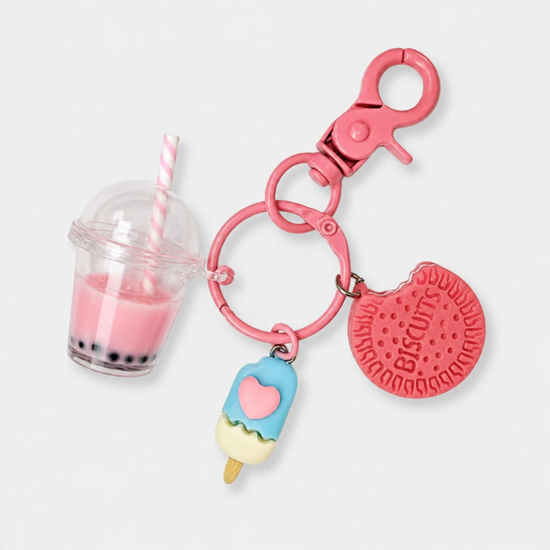 Josh & Tate - BubbleBite™ Milk Tea Keychain - A pink metal keychain with a lobster clasp, featuring three charms: a miniature pink drink with a striped straw, a blue and cream popsicle with a pink heart, and a pink biscuit-shaped charm embossed with 'Biscoff'.