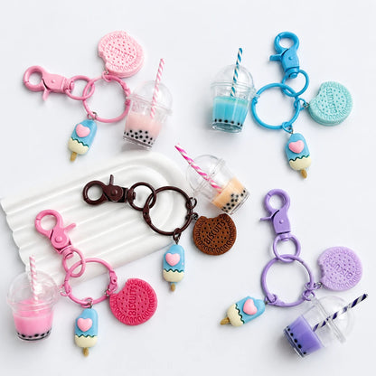 Josh & Tate - BubbleBite™ Milk Tea Keychain - Six colorful boba tea keychains arranged on a white background, each with a clasp, straw, cup, ice cream cone, and round cookie charm in pink, blue, brown, and purple.