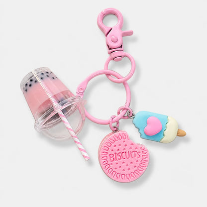 Josh & Tate - BubbleBite™ Milk Tea Keychain - A pink silicone keychain bag charm set featuring a boba tea cup, a round biscuit-shaped charm with 'BISCUITS' embossed, and a popsicle charm with a pink heart, all attached to a pink lobster clasp on a light gray background.