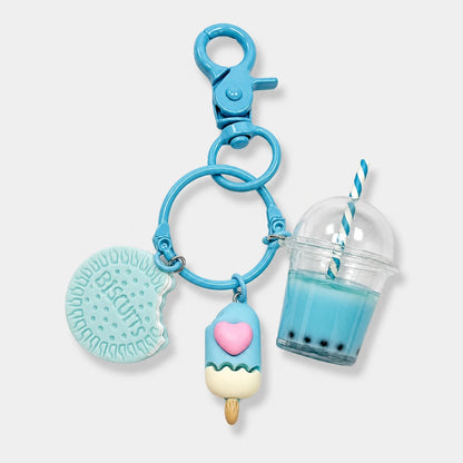 Josh & Tate - BubbleBite™ Milk Tea Keychain - A light blue keychain featuring three charms: a biscuit-shaped charm with the word 'Biscuits' embossed, a popsicle charm with a pink heart, and a miniature boba tea cup with a blue-and-white striped straw, all attached to a blue clasp on a light gray background.