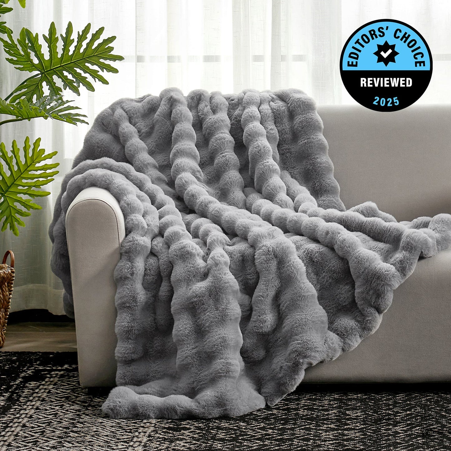 Gray textured blanket draped over a sofa with a plant and rug in the background, featuring an 'Editors' Choice' badge.