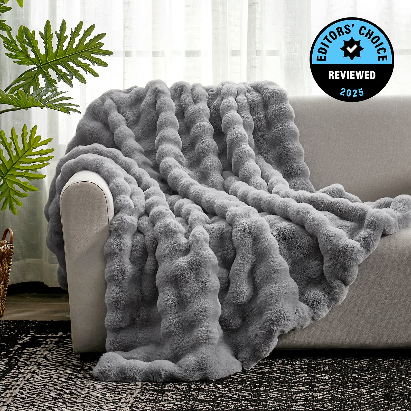 Gray textured blanket draped over a sofa with a plant and rug in the background, featuring an 'Editors' Choice' badge.