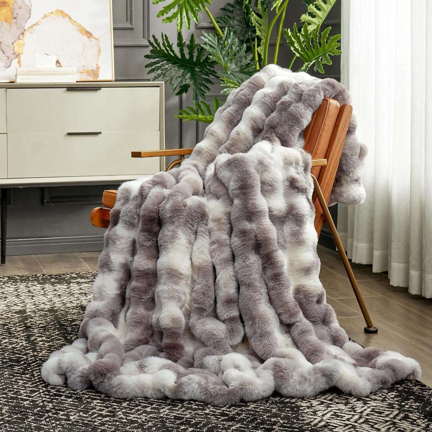 Gray fuzzy blanket draped over a chair in a living room setting with plants and furniture.