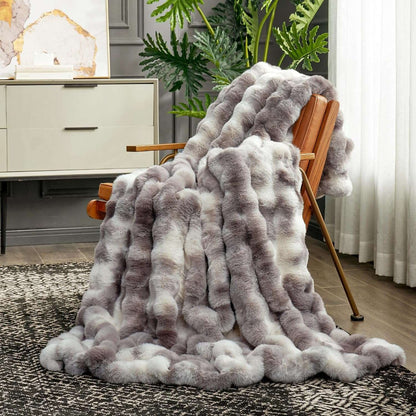 Gray fuzzy blanket draped over a chair in a living room setting with plants and furniture.