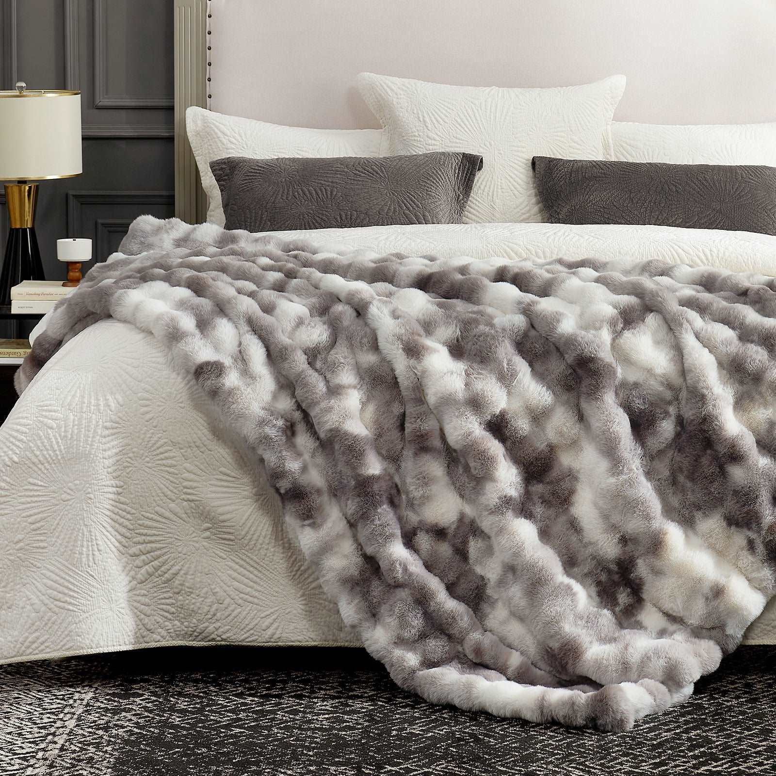 Gray textured blanket on a bed with white bedding and pillows in a bedroom setting.