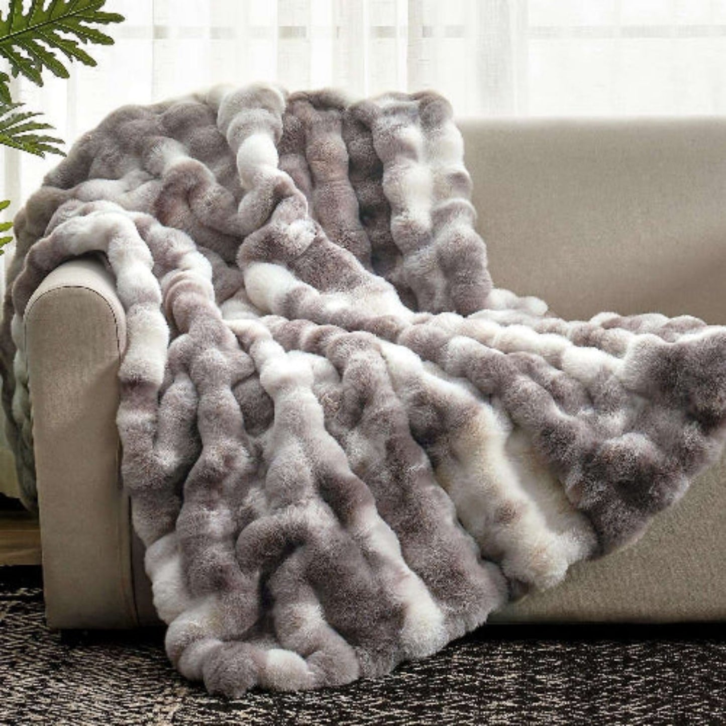 Fluffy gray and white blanket draped over a beige sofa with a neutral background