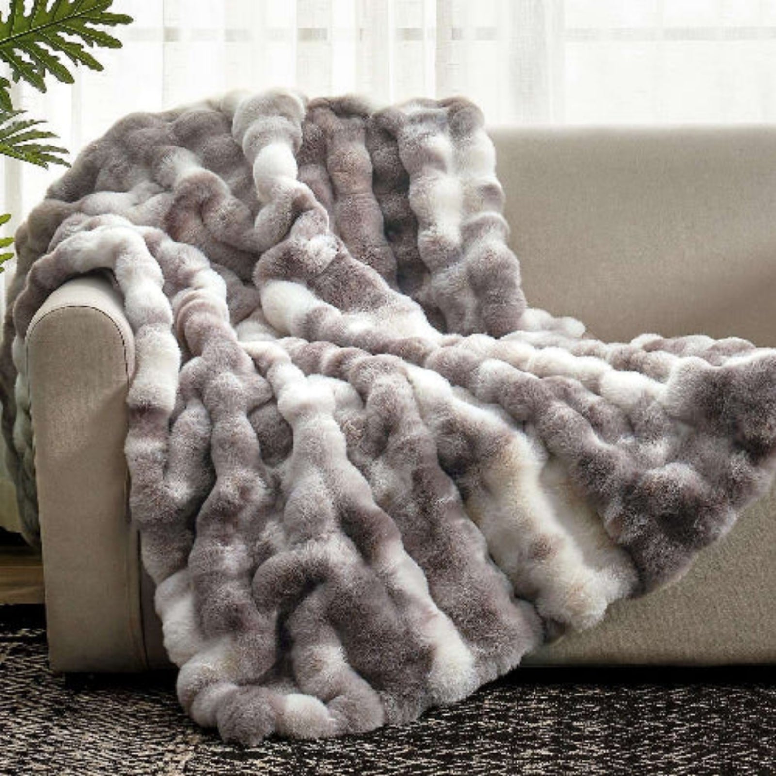 Fluffy gray and white blanket draped over a beige sofa with a neutral background