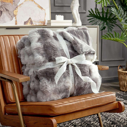 Gray fuzzy blanket with a white ribbon on a brown leather chair in a cozy room.