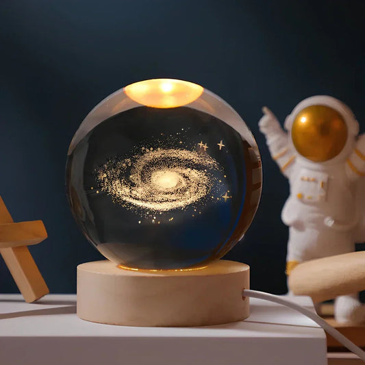 Glass ball with galaxy design on a wooden base, next to an astronaut figurine.