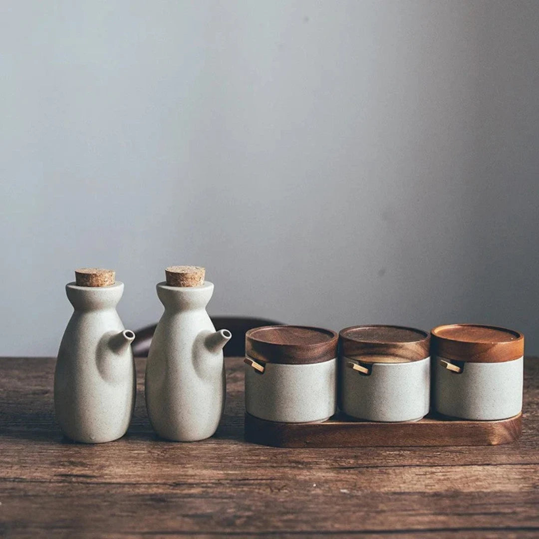 Josh & Tate - Ceramic Condiment Storage Set - Two ceramic bottles with cork stoppers and three wooden-lidded containers on a wooden surface.