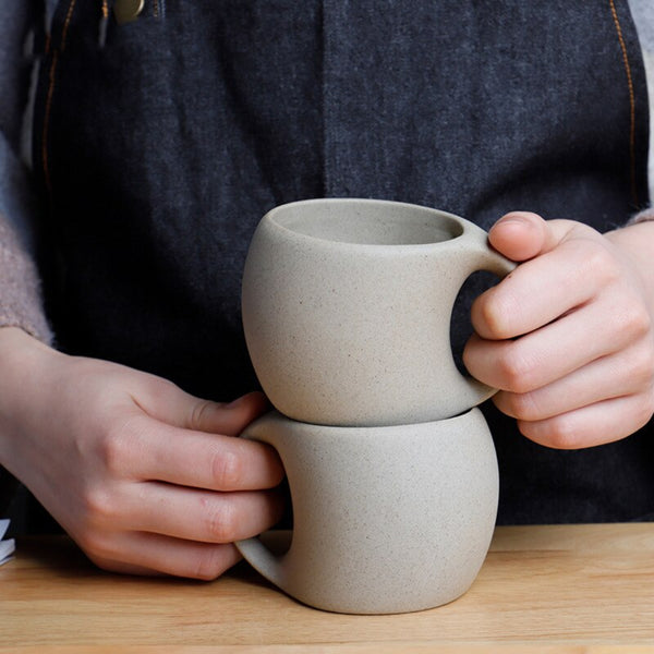 Person holding two stacked ceramic mugs on a wooden surface